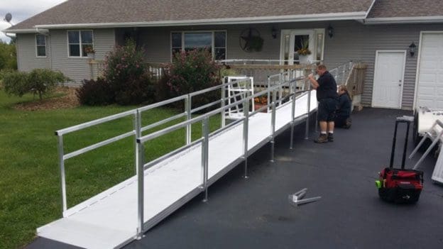Two people assemble a metal wheelchair ramp from the driveway to the ...