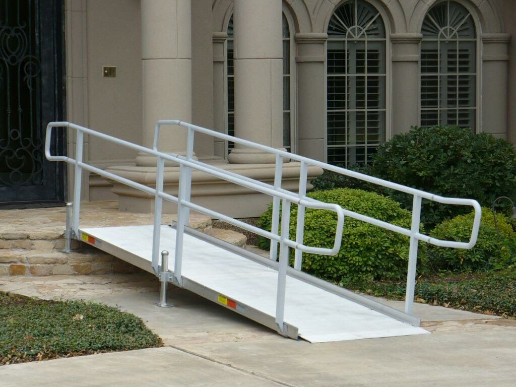 A metal wheelchair ramp with handrails leads from a sidewalk to the ...