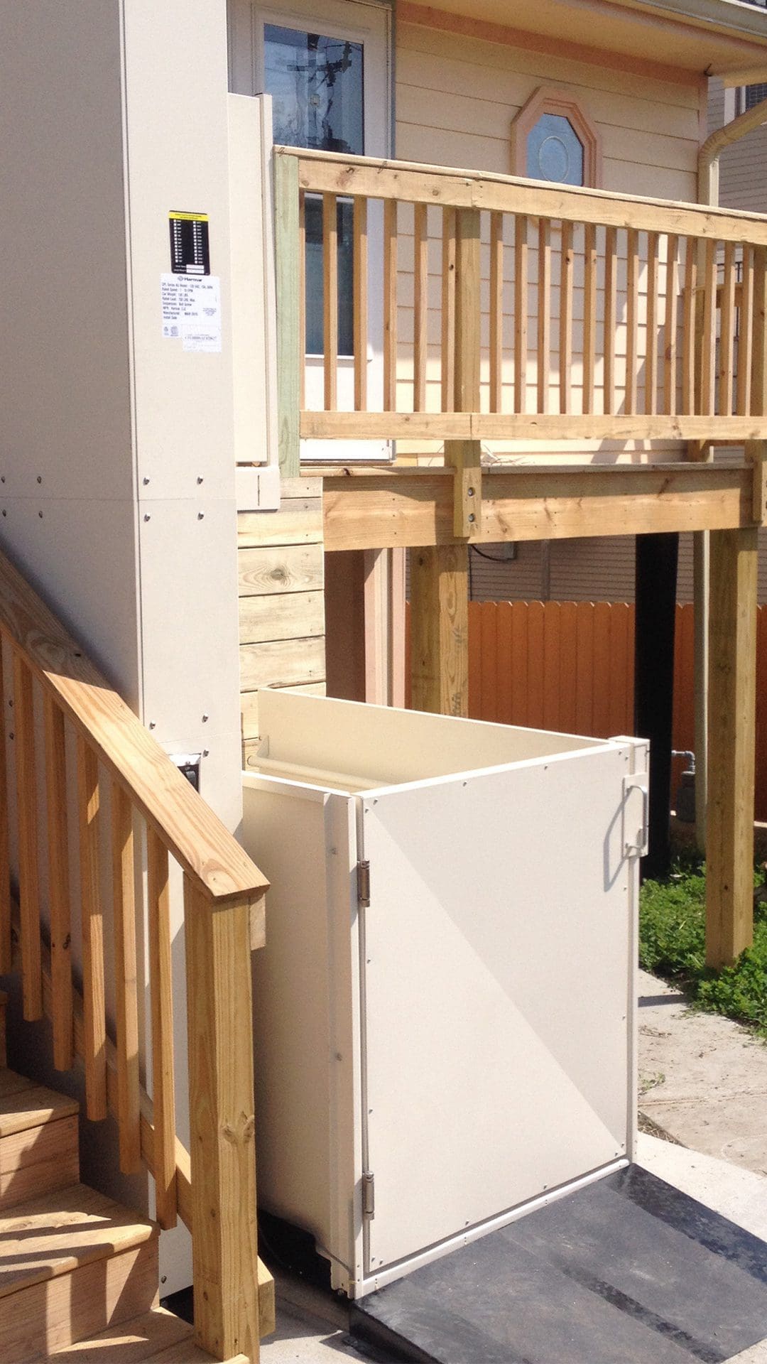 A vertical platform lift is installed beside a wooden porch, providing ...