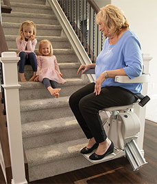 Women on Straight Stair Lift with Grand Children Sitting on Stairs in Bloomington, Kankakee, Peoria, Chicagoland, Schaumburg, and Sheboygan