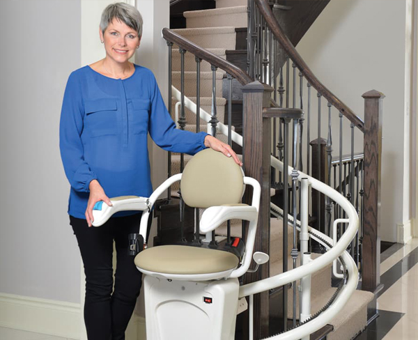 Lady Standing by Stairs with a Curved Stairlifts in Naperville, IL, Kenosha, Lake Geneva, Racine, Chicagoland, Downers Grove, IL