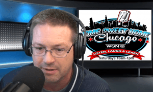 A man wearing glasses and headphones speaks into a microphone in a radio studio. Behind him is a screen displaying the Home Sweet Home Chicago WGN Radio 720 logo and show details.