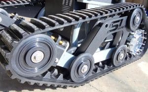 Close-up view of a black rubber track system with visible wheels and metal components on a concrete surface, likely part of a robotic or industrial vehicle.