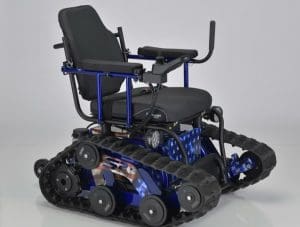 A motorized wheelchair with tank-like rubber tracks instead of wheels, designed for off-road or rugged terrain, featuring a padded seat, armrests, and a blue frame.