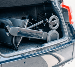 A folded electric wheelchair placed in the trunk of a car, showing its compact size and portability for easy transportation.