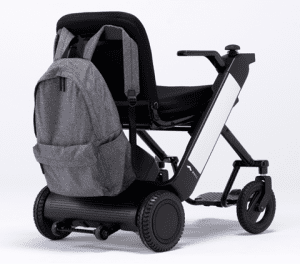 A compact, modern mobility scooter with a black frame and seat. A gray backpack is hanging on the backrest. The scooter has small wheels and a sleek, minimalist design, photographed against a plain white background.