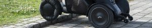 A close-up of a modern wheelchair with large, specialized wheels smoothly climbing a curb from a paved walkway onto a grassy area.