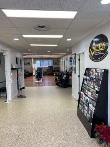 A well-lit showroom with mobility scooters, brochures on a display rack, seating, and a large Access Mobility sign on the wall. The space is clean, organized, and has light-colored walls and flooring.