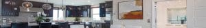 Modern kitchen and dining area with dark wood cabinets, stainless steel appliances, white countertops, pendant lights, a large abstract painting on the wall, and a partially open door revealing a bright hallway.