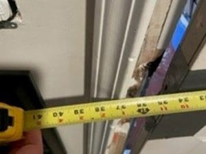 A hand holds a yellow tape measure extended across a partially open wall, showing a measurement of about 41 inches. The wall appears to be under construction or renovation.