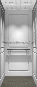 Interior view of a modern residential elevator with white paneled walls, a metallic handrail on the back wall, recessed ceiling lights, and a gray textured floor.