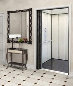 A modern home elevator with open doors is next to a console table with a lamp, a flower vase, and a large framed mirror on the wall above. The floor is tiled in white with brown diamond patterns.