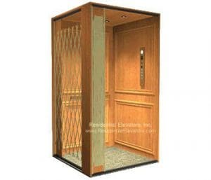 A residential elevator with wood-paneled walls, a metal accordion-style safety gate, soft overhead lighting, and a simple control panel on the side wall.