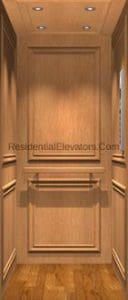 A residential elevator interior with paneled wooden walls, a wooden floor, recessed ceiling lights, and a simple handrail on the back wall.