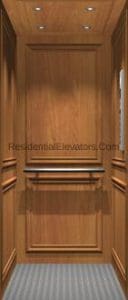 Interior of a residential elevator with wood-paneled walls, decorative molding, a handrail, gray patterned flooring, and recessed ceiling lights.