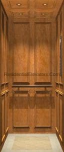 Wood-paneled residential elevator interior with recessed lighting, decorative wall trim, and a light-colored floor.