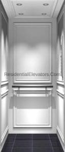 Elegant residential elevator interior with white paneled walls, decorative molding, dark tiled floor, recessed ceiling lights, and a metallic rail along the back wall.