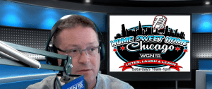 A man wearing glasses speaks into a microphone in a radio studio. Behind him is a sign for Home Sweet Home Chicago on WGN Radio 720, advertising the show airing Saturdays from 10 a.m. to 1 p.m.