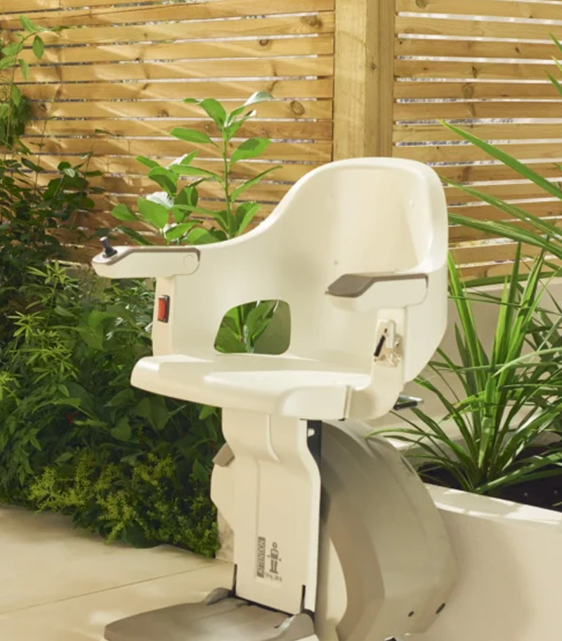 Access BDD HomeGlide Outdoor Straight Stair Lift with Concrete Ledge and Planted Garden in Background