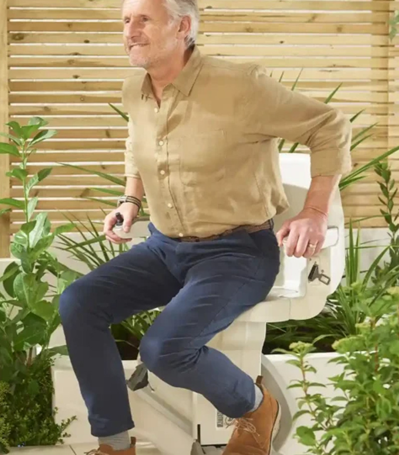 Rider Transferring To or From Access BDD HomeGlide Outdoor Straight Stair Lift with Plants and Flowers in Background