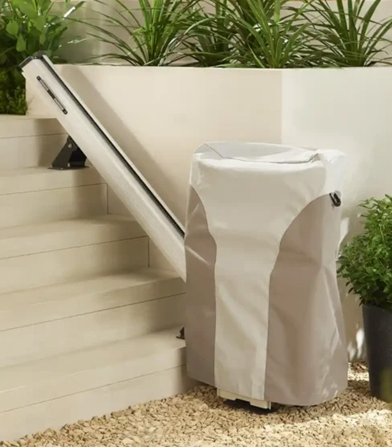 Access BDD Outdoor Straight Stair Lift with Weather Cover Mounted to Concrete Steps with Wall and Green Plants in Background
