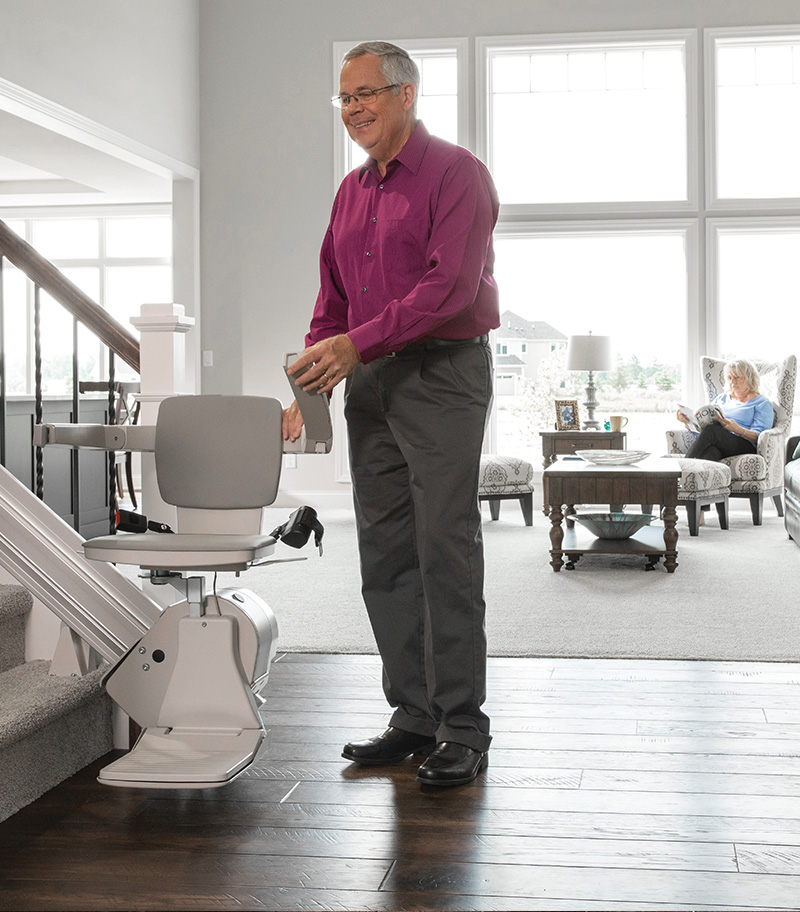 Owner Demonstrating Ease of Folding Up Armrest on Bruno Elan Straight Stairlift at Bottom of Stairs