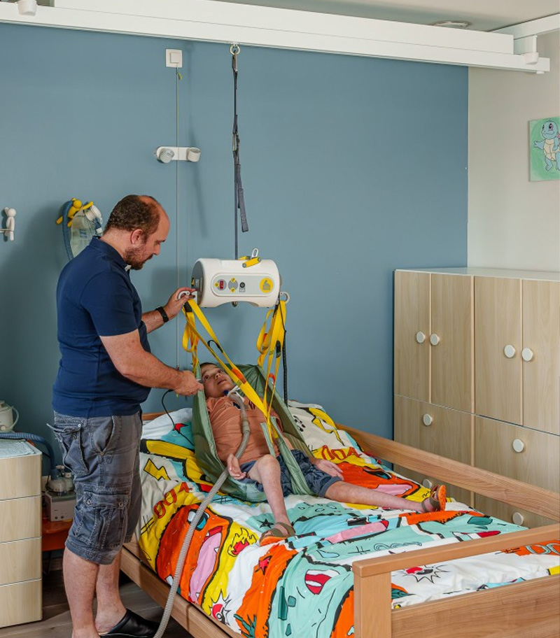 Father helping disabled son to bed with SureHands portable ceiling lift and sling