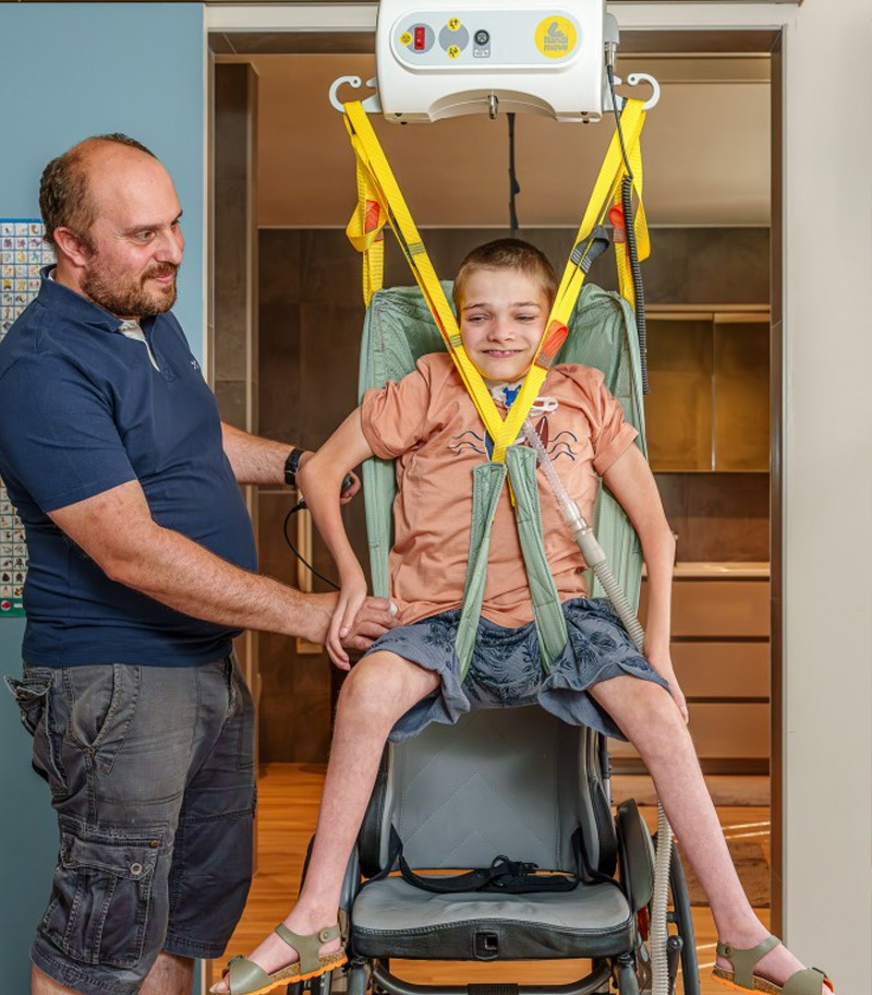 Father assisting disabled son with transfer by using a portable ceiling lift from SureHands