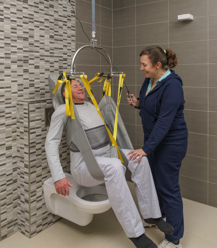 Caregiver is easily and safely assisting client in transfer to toilet with SureHands fixed ceiling lift and hygienic sling