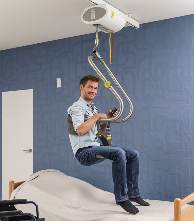 Happy client using a fixed ceiling lift with SureHands Body Support to transfer Independently between wheelchair and bed