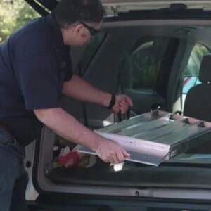 A person loads a folded Bi-Fold Portable Wheelchair Ramp by National Ramp into the back of an SUV with the rear door open.