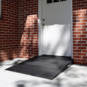 A black Rubber Threshold Ramp by National Ramp leads up to a white door in a red brick wall, providing accessible entry to the building.