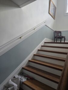 White stairlift rail installed along a short residential staircase with dark wood steps, white trim, and light gray walls, demonstrating a compact accessibility solution for navigating changes in floor level.
