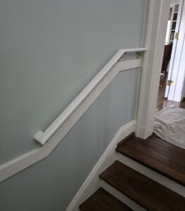 White stairlift rail installed along a short residential staircase with dark wood steps, white trim, and light gray walls, demonstrating a compact accessibility solution for navigating changes in floor level.