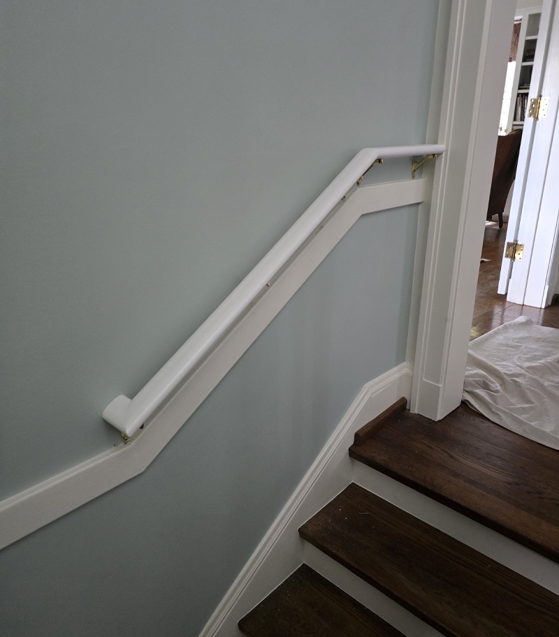 White stairlift rail installed along a short residential staircase with dark wood steps, white trim, and light gray walls, demonstrating a compact accessibility solution for navigating changes in floor level.
