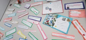 A bulletin board displays numerous colorful, handwritten notes and printed messages, including Elevator Service Testimonials. Cards and papers, some with decorative borders and stickers, are arranged in a scattered, overlapping pattern on the board.