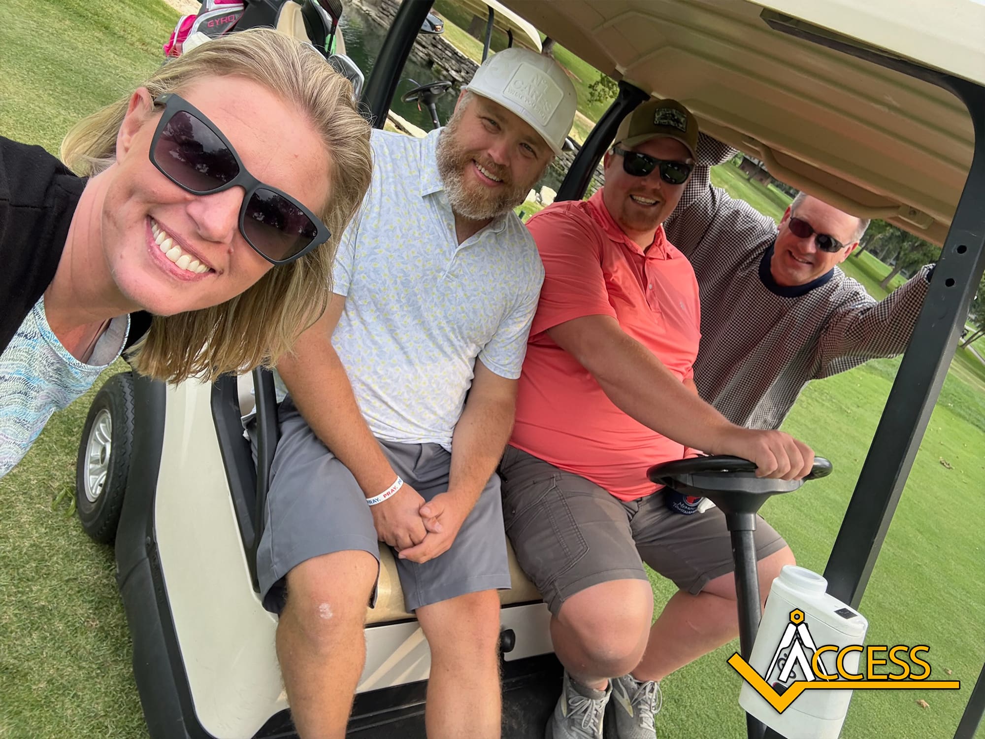 Four people smile for a selfie by a golf cart on a grassy golf course. Three men sit in the cart, one holding the steering wheel, while a woman stands nearby. A yellow Access logo is in the bottom right corner.