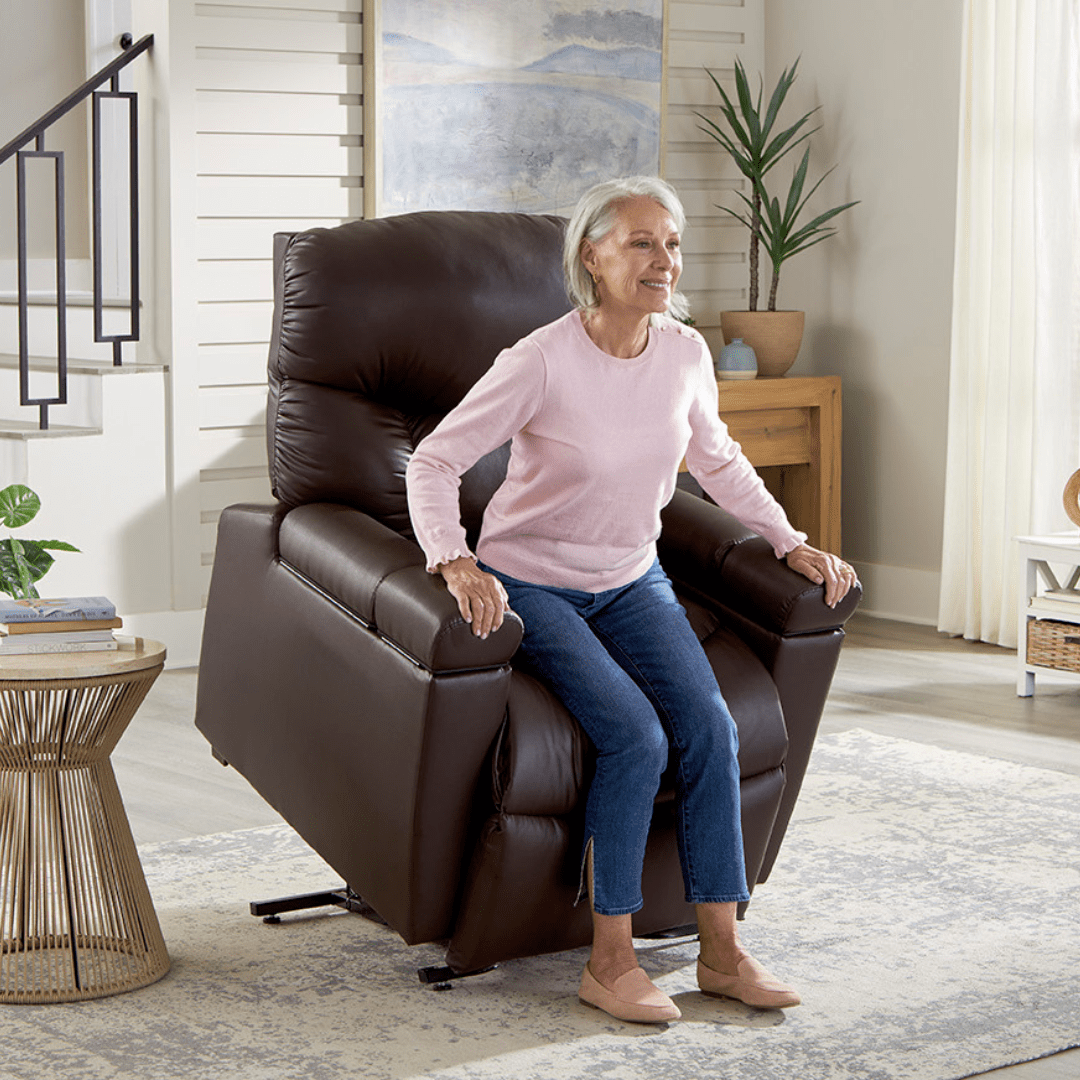 An older woman in a pink sweater and blue jeans uses the Cloud+ Large - Lift Chair by Golden Technologies to help her stand in a bright, modern living room. An older woman in a pink sweater and blue jeans uses the Cloud+ Large - Lift Chair by Golden Technologies to help her stand in a bright, modern living room.