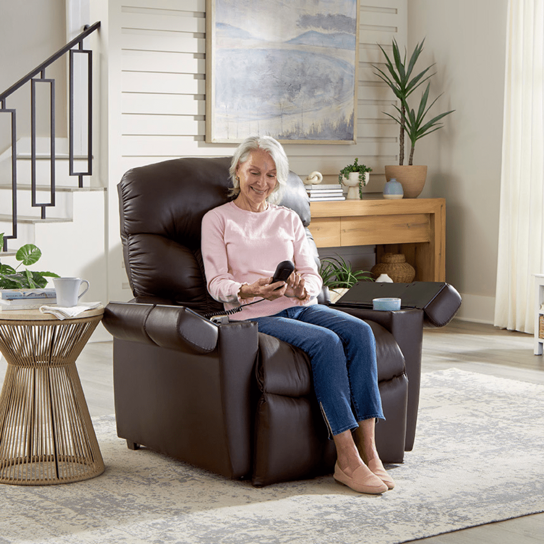 An older woman relaxes in a well-lit, modern living room, smiling as she sits comfortably in the Cloud+ Small - Lift Chair by Golden Technologies, holding its remote control. Lush plants and a large framed painting decorate the cozy space behind her. An older woman relaxes in a well-lit, modern living room, smiling as she sits comfortably in the Cloud+ Small - Lift Chair by Golden Technologies, holding its remote control. Lush plants and a large framed painting decorate the cozy space behind her.
