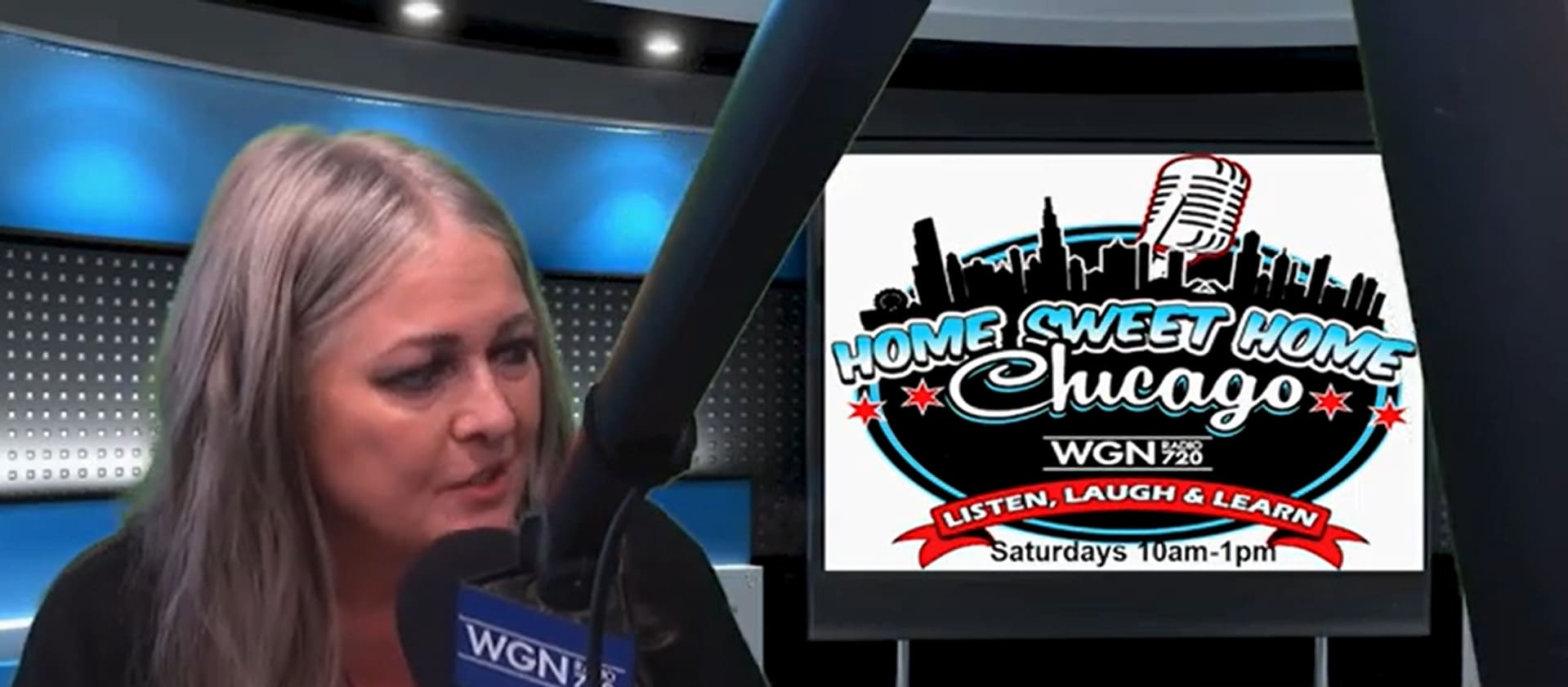 A woman with long gray hair speaks into a microphone in a radio studio. Next to her is a screen displaying the Home Sweet Home Chicago show logo, airing Saturdays 10am-1pm on WGN 720.
