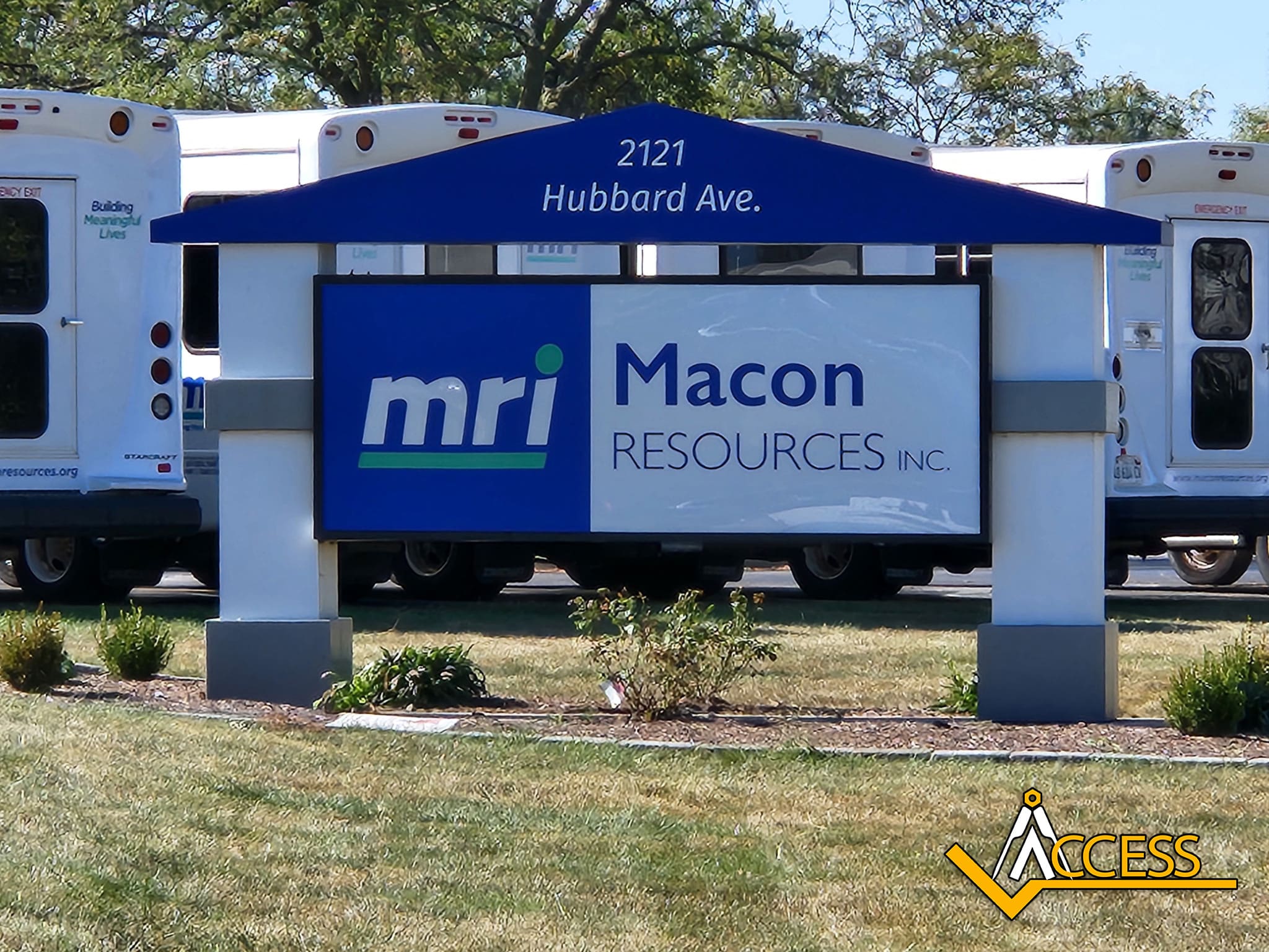 A sign for Macon Resources Inc. (mri) at 2121 Hubbard Ave. stands on a lawn, with white ACCESS public transit vans parked in the background.