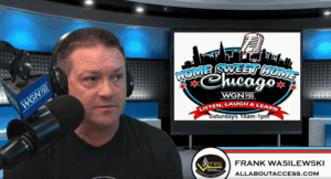 A man sits in front of a microphone in a radio studio. Behind him is a screen with the “Home Sweet Home Chicago” show logo and schedule. A nameplate reads “Frank Wasilewski, All About Access.”.