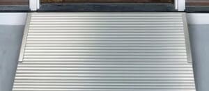 A metal wheelchair ramp with horizontal ridges leads up to a doorway, providing accessible entry. The ramp is clean and positioned securely against the threshold.