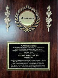 A wooden plaque with a gold circular emblem at the top reading BRUNO. Below, a gold plate honors Access Elevator Inc with the Platinum Award for outstanding achievement from Bruno Independent Living Aids in 2012.