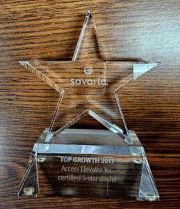 A clear, star-shaped glass award on a wooden surface, engraved with Savaria and TOP GROWTH 2017 Access Elevator Inc. certified 5-star dealer.