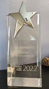 A clear glass award with a silver star on top, engraved with savaria Top Sales, ACCESS ELEVATOR INC, Certified 5-Star Dealer, 2022. The award stands on a dark surface against a light background.