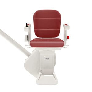 The Freecurve Curved Stair Lift by Handicare is a red and white motorized stair chair with armrests, mounted on a rail, designed to help people with mobility challenges move safely up and down stairs.