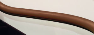 A Handicare Freecurve Curved Stair Lift with a brown, cylindrical handrail is mounted on a light wall, curving gently—typical of curved stair lift installs. The image’s lower area appears dark, possibly due to shadow or surface color.