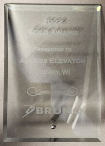 A glass plaque engraved with 2022 Gold Award Presented to Access Elevator Cudahy, WI and featuring the Bruno company logo at the bottom. The plaque is mounted on a wall.