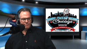 A man wearing glasses and a black shirt speaks into a WGN Radio microphone in a studio. Behind him, a screen displays the Home Sweet Home Chicago show logo and broadcast details for Saturdays from 10am to 1pm.